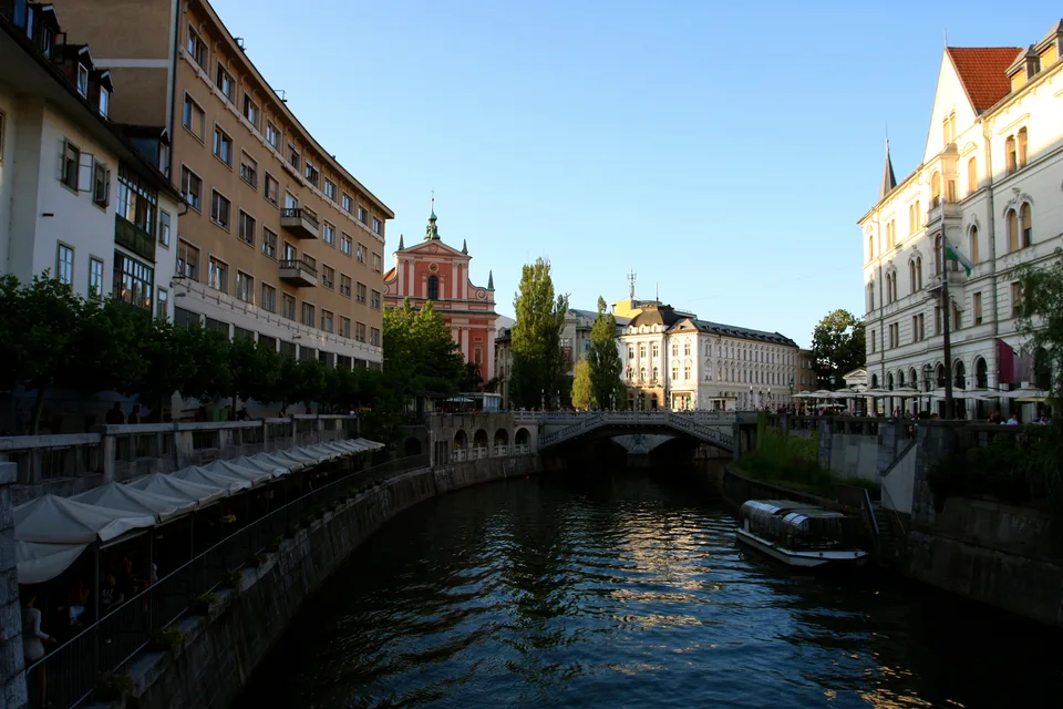 Ljubljanica med starimi mestnimi pročelji s Tromostovjem in frančiškansko cerkvijo v ozadju.